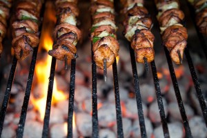 Mixes sheesh kabobs on the grill with charcoal and flames
