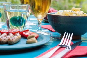 Outside table setting with meat and tomatoes, wine and beverages and a bowl of macaroni and cheese